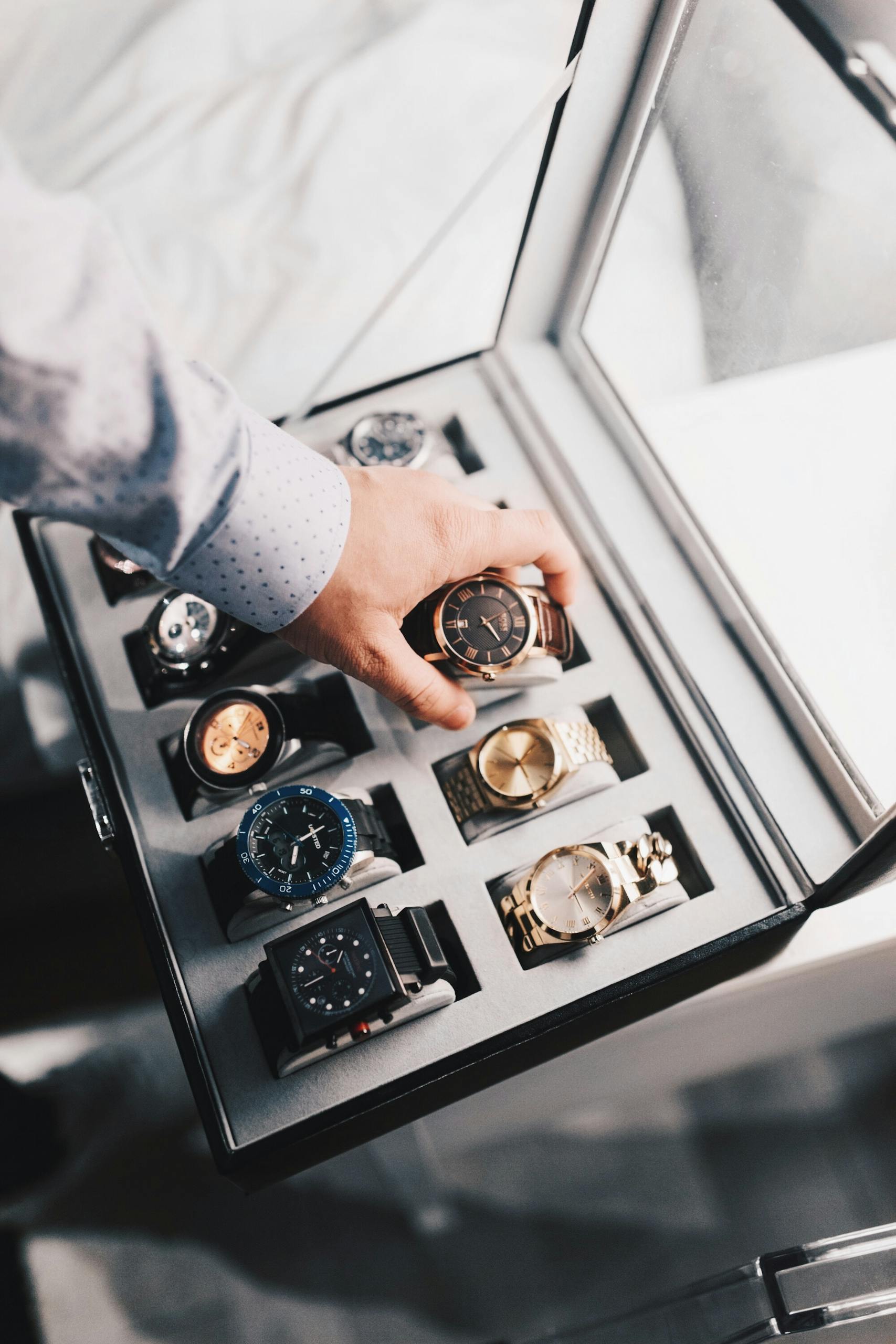 Photo by Mister Mister A sophisticated display of luxury watches in an elegant case with a hand selecting one.